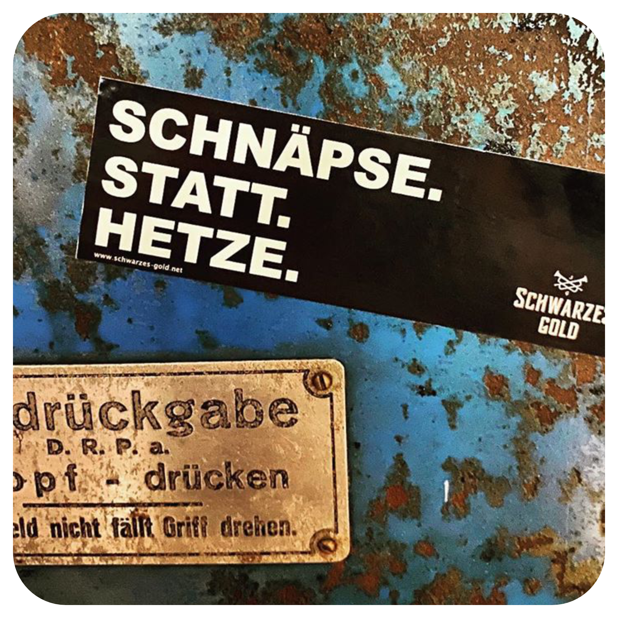 Sticker mit Aufschrift ‚Schnäpse statt Hetze‘ auf einer rostigen blauen Metallfläche, auffälliger Slogan.