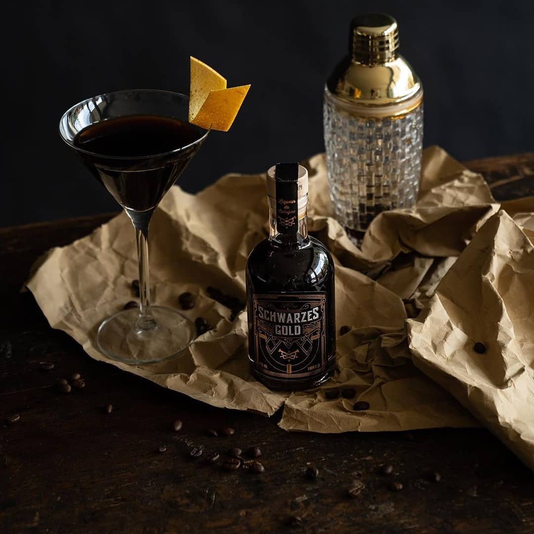 Schwarzes Gold Espresso-Likör Flasche neben einem Espresso-Martini mit Orangenzeste und Cocktail-Shaker, ideal für hochwertige Kaffeelikör-Cocktails aus Bio-Fairtrade-Kaffee.